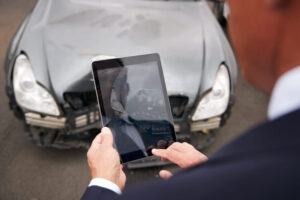 Car Accident Victim Taking Picture With Digital Tablet Of Damage To Car From Motor Accident